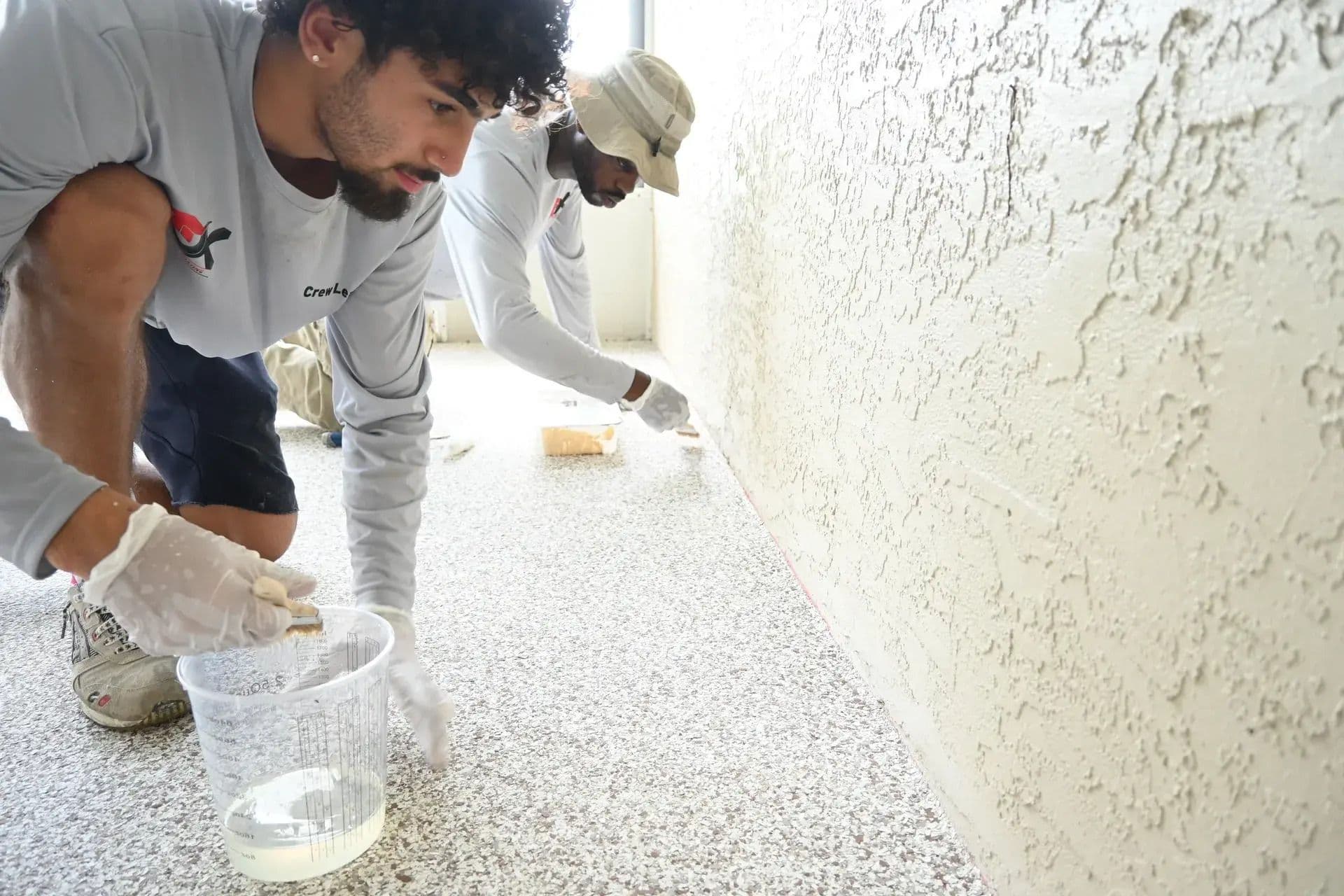 Flooring contractors carefully applying a protective topcoat to a newly resurfaced concrete